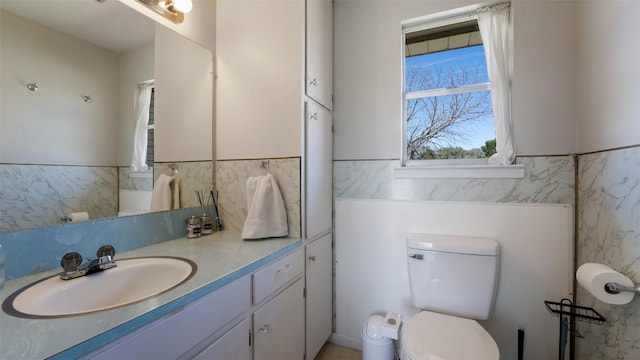 bathroom featuring tile walls, wainscoting, vanity, and toilet