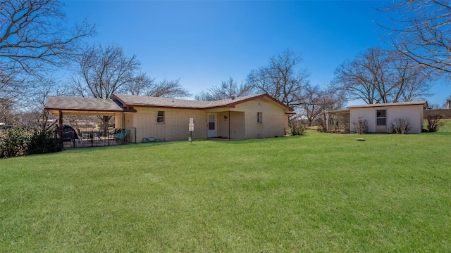 rear view of property with an outdoor structure, brick siding, an attached carport, and a yard