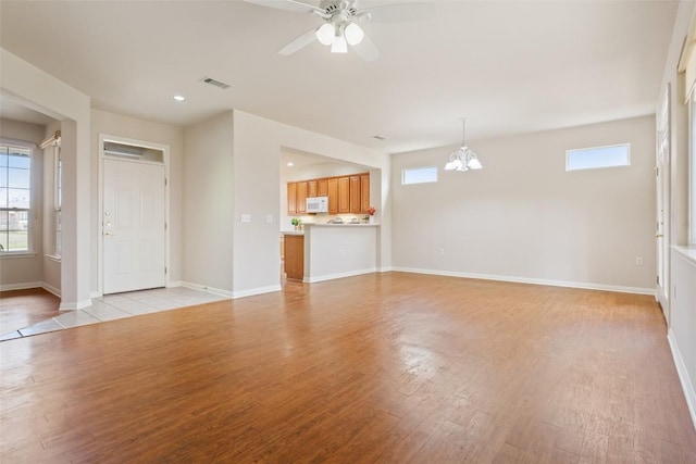 unfurnished living room featuring light wood finished floors, visible vents, baseboards, ceiling fan with notable chandelier, and recessed lighting