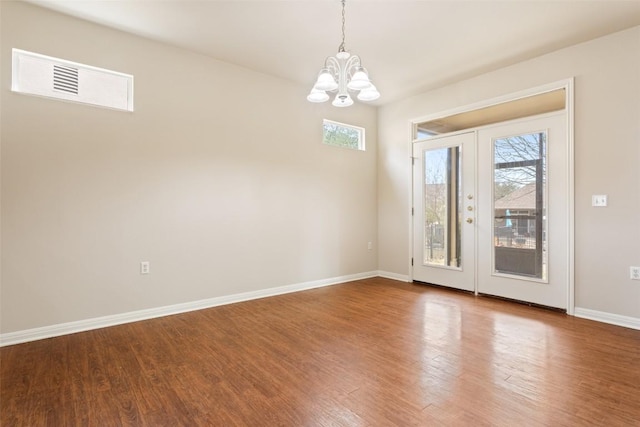 spare room featuring wood finished floors, baseboards, visible vents, french doors, and a notable chandelier