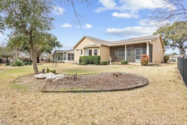 rear view of property featuring stucco siding, a lawn, fence, and a sunroom