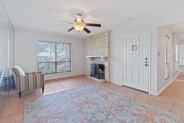 unfurnished living room with tile patterned flooring, baseboards, a ceiling fan, and a stone fireplace