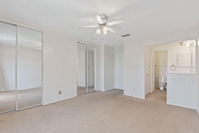 unfurnished bedroom with baseboards, visible vents, light colored carpet, ceiling fan, and two closets