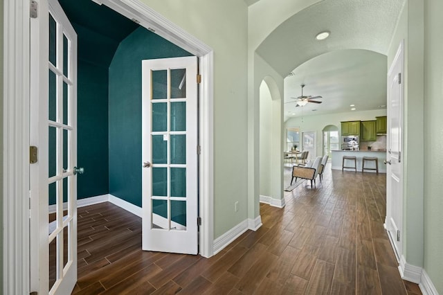 hallway with arched walkways, french doors, dark wood-style floors, and baseboards