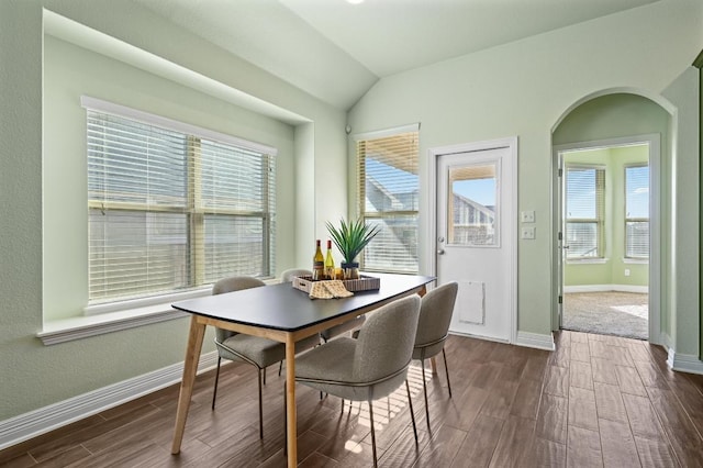 dining area with dark wood-type flooring, arched walkways, vaulted ceiling, and baseboards