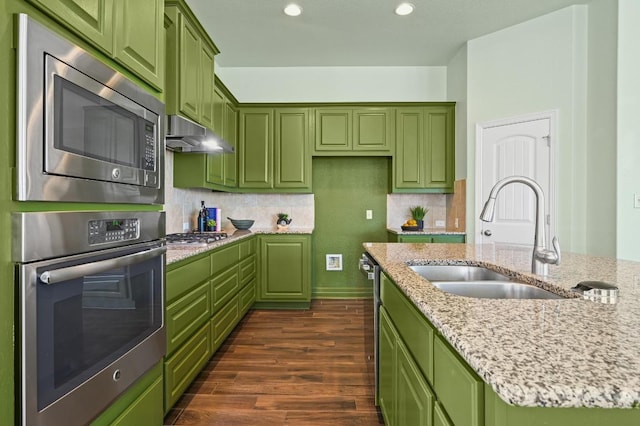 kitchen with dark wood-type flooring, a sink, stainless steel appliances, under cabinet range hood, and green cabinetry