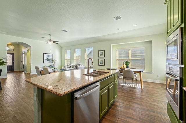 kitchen featuring arched walkways, green cabinetry, appliances with stainless steel finishes, dark wood-type flooring, and a sink