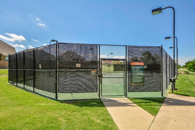 view of tennis court with a gate, fence, and a lawn