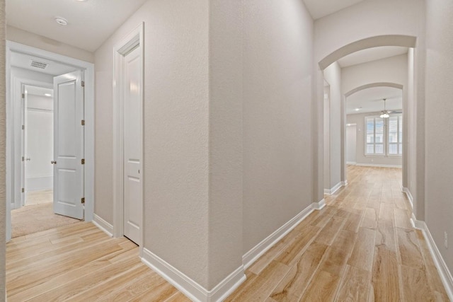 corridor with arched walkways, light wood-type flooring, visible vents, and baseboards