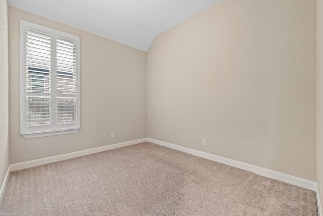 carpeted spare room with vaulted ceiling and baseboards