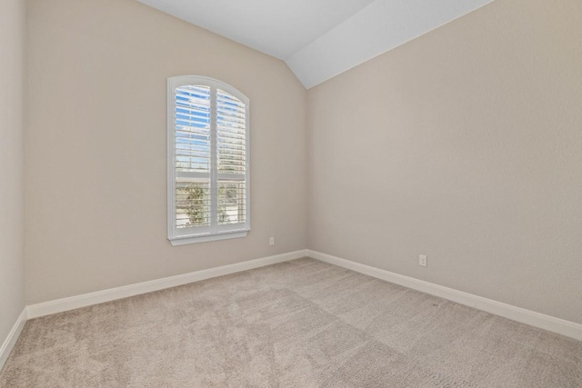 empty room featuring baseboards, vaulted ceiling, and light colored carpet