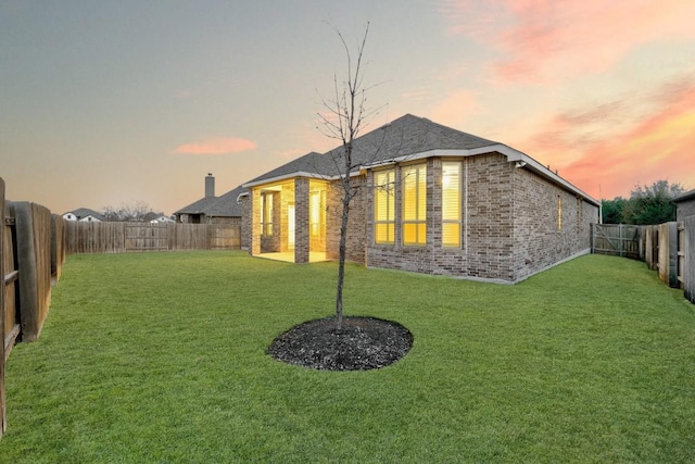 back of property at dusk with a yard, a fenced backyard, and brick siding