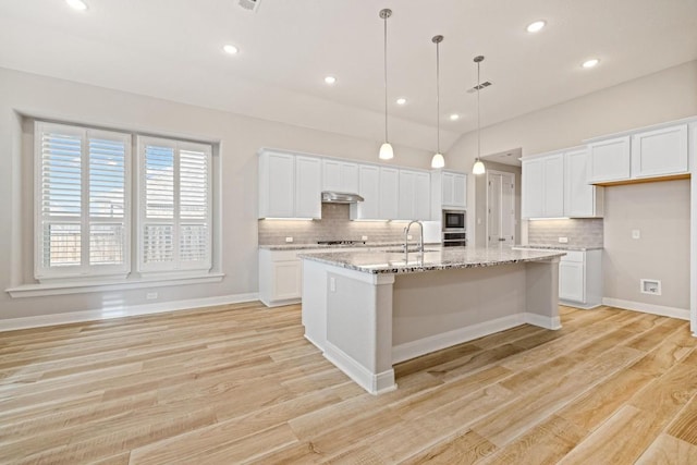 kitchen featuring stainless steel appliances, white cabinets, a sink, an island with sink, and light wood-type flooring