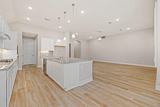 kitchen featuring light wood finished floors, arched walkways, a sink, a kitchen island with sink, and backsplash