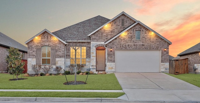 french provincial home with driveway, a shingled roof, a lawn, stone siding, and brick siding