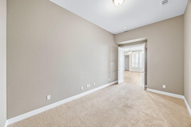 spare room with baseboards, a textured wall, visible vents, and light colored carpet