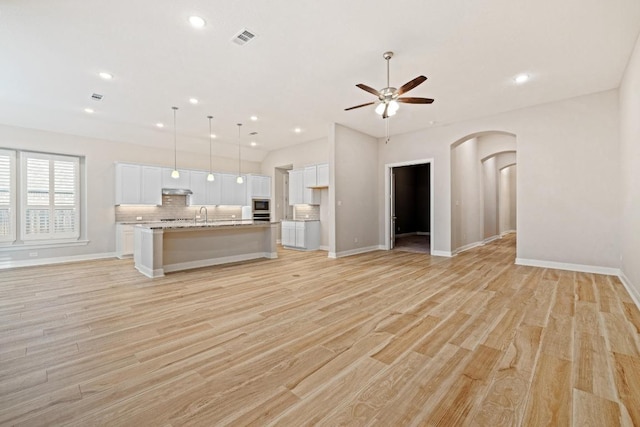 unfurnished living room featuring arched walkways, light wood-style flooring, visible vents, and a ceiling fan