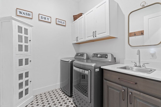 laundry room featuring baseboards, light floors, washer and dryer, cabinet space, and a sink