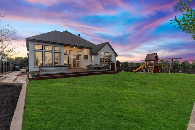 back of house at dusk featuring a yard, a deck, a fenced backyard, and a playground