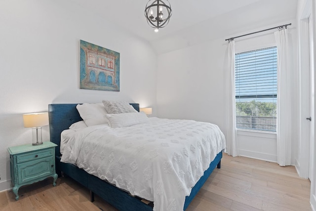 bedroom featuring lofted ceiling, a notable chandelier, light wood-style floors, and baseboards