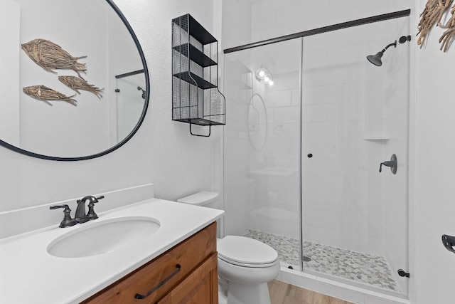 bathroom with a stall shower, toilet, vanity, and wood finished floors