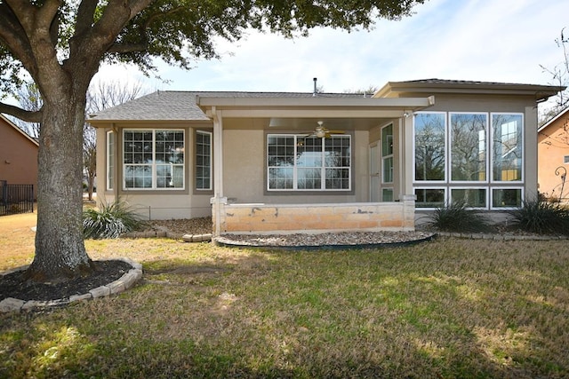 back of property with stucco siding, a yard, and ceiling fan