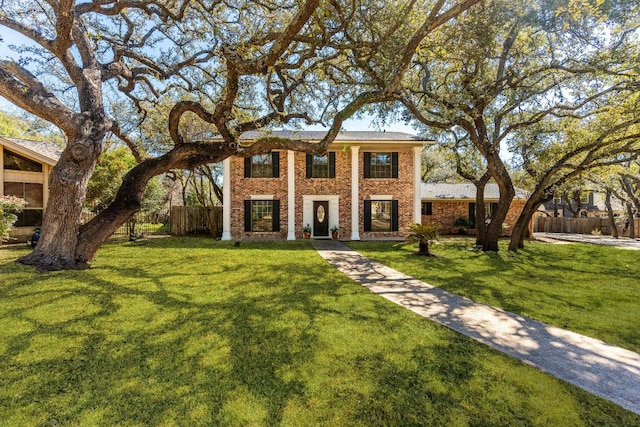 neoclassical / greek revival house with brick siding, a front yard, and fence