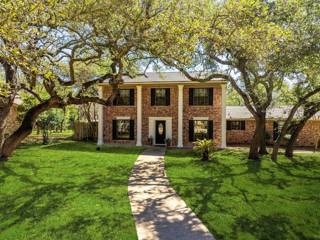 greek revival inspired property with a front lawn, fence, and brick siding