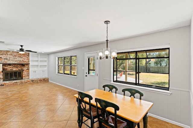 7701 Penelope Cir, Austin, TX 78759 - dining space with built in shelves, a brick fireplace, light tile patterned floors, and ceiling fan with notable chandelier