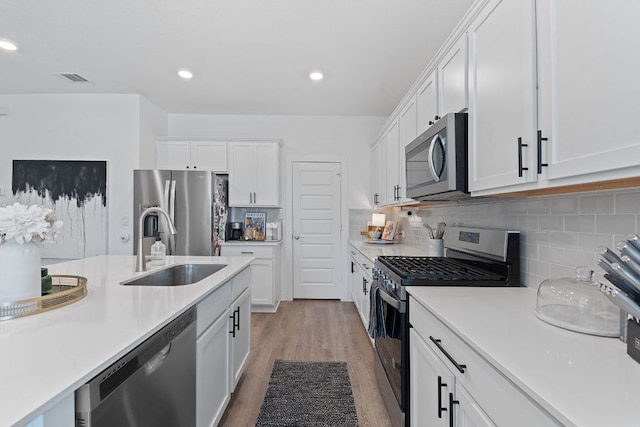 kitchen featuring light wood-style flooring, stainless steel appliances, a sink, white cabinets, and light countertops