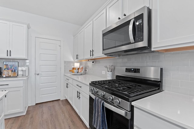 kitchen with light wood finished floors, light countertops, backsplash, appliances with stainless steel finishes, and white cabinets