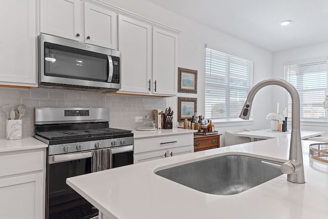 kitchen with white cabinets, a sink, stainless steel appliances, light countertops, and backsplash