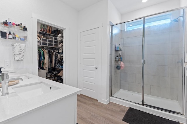 bathroom featuring double vanity, a stall shower, a sink, and wood finished floors