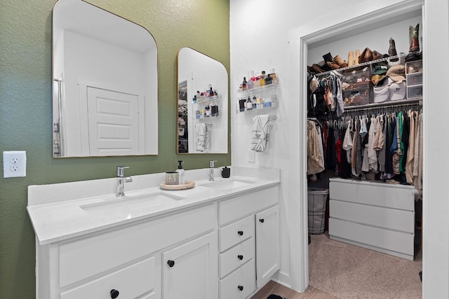 bathroom with a textured wall, a walk in closet, a sink, and double vanity