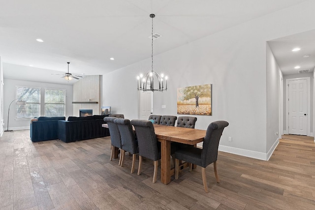 dining space featuring baseboards, visible vents, a tiled fireplace, ceiling fan, and wood finished floors