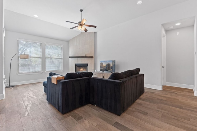 living area featuring ceiling fan, a large fireplace, wood finished floors, baseboards, and vaulted ceiling