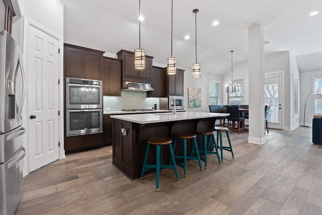 kitchen with lofted ceiling, appliances with stainless steel finishes, range hood, light countertops, and backsplash