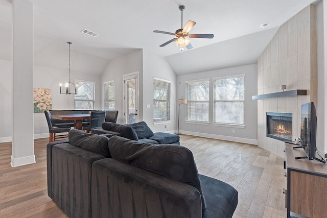 living area with vaulted ceiling, a tiled fireplace, visible vents, and light wood-style floors