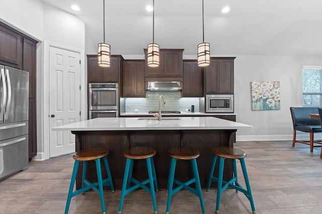 kitchen with decorative backsplash, a breakfast bar area, appliances with stainless steel finishes, ventilation hood, and light countertops