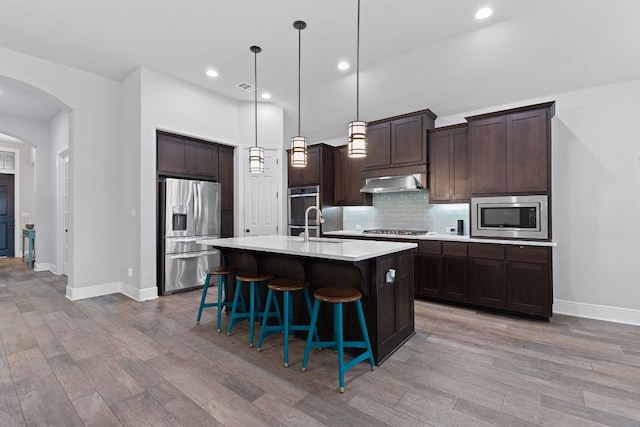 kitchen featuring arched walkways, under cabinet range hood, stainless steel appliances, light countertops, and tasteful backsplash