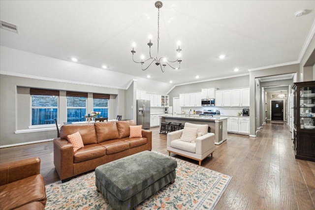 living room featuring visible vents, crown molding, light wood finished floors, and an inviting chandelier