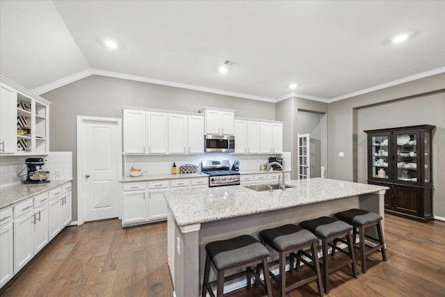 kitchen featuring open shelves, stainless steel appliances, white cabinetry, a sink, and a kitchen bar