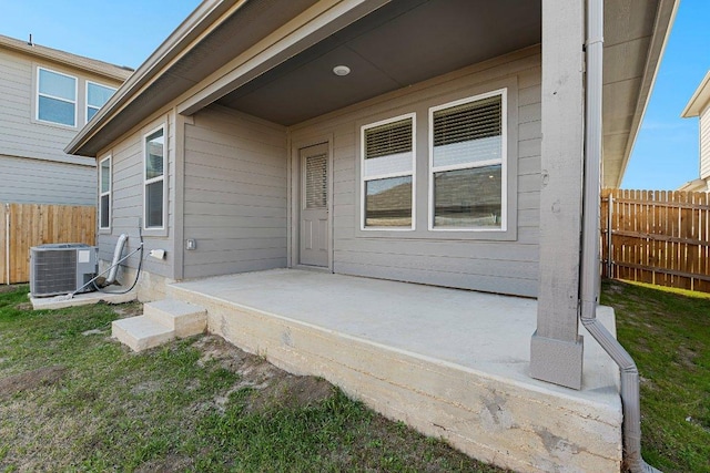 view of exterior entry with a patio area, fence, and central AC unit