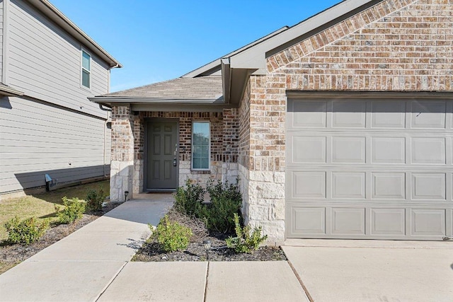 doorway to property with an attached garage, stone siding, roof with shingles, and brick siding