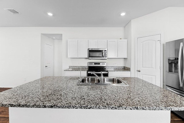 kitchen featuring stainless steel appliances, dark stone counters, visible vents, and a sink