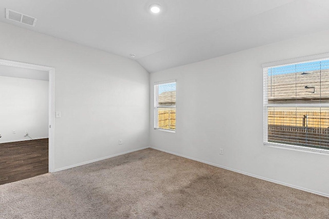 spare room with vaulted ceiling, carpet floors, and visible vents