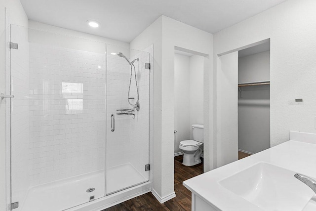 full bath featuring a stall shower, toilet, wood finished floors, a spacious closet, and vanity