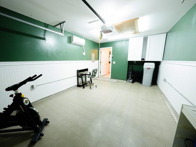 workout area featuring a wainscoted wall, a garage, light floors, a wall mounted air conditioner, and attic access