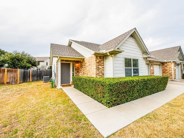 single story home featuring roof with shingles, fence, a front lawn, central AC, and brick siding