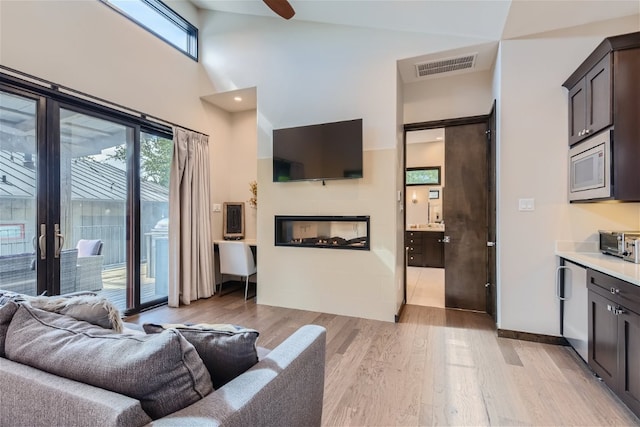 living room with light wood finished floors, a toaster, visible vents, a glass covered fireplace, and high vaulted ceiling